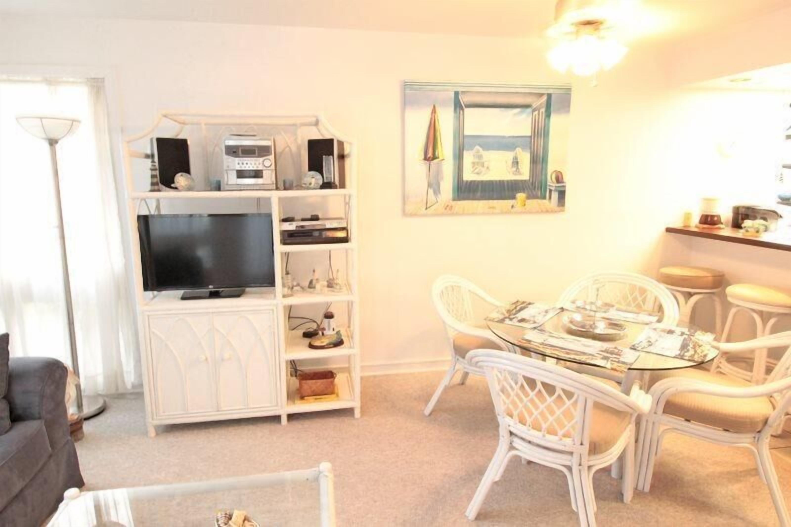 A living room with a flat-screen TV, white shelving unit, dining table with chairs, and a framed picture on the wall.