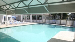 Une piscine intérieure à l’eau d’un bleu cristallin, entourée de chaises longues et d’un espace abrité doté d’un toit en verre.