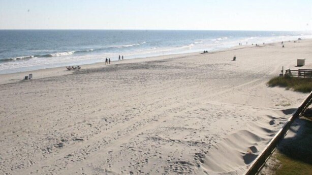 Une vaste plage de sable où l’on aperçoit quelques personnes et quelques constructions.