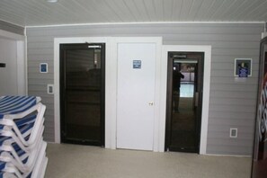 A room with two doors, one leading to a balcony and the other to a hallway. There is a stack of striped chairs in the foreground.