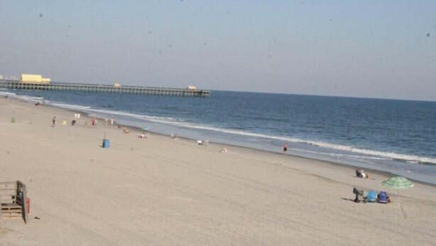 A beach with a pier extending into the water, sandy beach, and a lifeguard stand. - Lake Arrowhead Fiesta (Myrtle Beach)