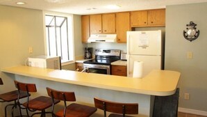 A compact kitchen with wooden cabinets, a central island with bar stools, a refrigerator, and a stove. - Lake Arrowhead Fiesta (Myrtle Beach)