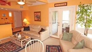 A living room with a beige sofa, a glass coffee table, a white chair, and a door labeled "TO THE BEACH". - Lake Arrowhead Den (Myrtle Beach)