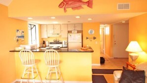 A compact kitchen with a central island, two bar stools, and a fish-themed wall decoration. - Lake Arrowhead Den (Myrtle Beach)