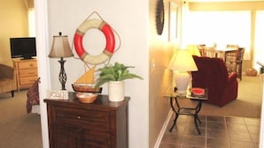 Una sala de estar con televisión, una lámpara, un sillón rojo y una zona de comedor con sillas y una mesa.
