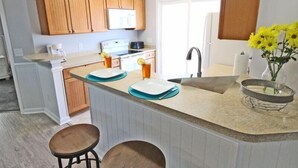 A kitchen with wooden cabinets, a white refrigerator, a sink, and a countertop with a vase of yellow flowers. - Lake Arrowhead Recess (Myrtle Beach)