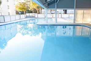 Ein Schwimmbecken mit überdachtem Bereich, umzäunt und neben einem Gebäude mit Balkon.