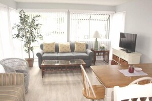 A living room with a sofa, a coffee table, a TV, and a dining table. - Lake Arrowhead Hearth (Myrtle Beach)