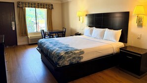 A hotel room with a bed, bedside table, lamp, and a window with curtains. - Castaic Inn Near Six Flags Magic Mountain (Castaic)