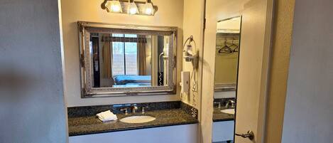 A bathroom with a large mirror, a sink, and a shower.