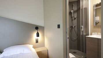 Una camera d'albergo con un letto, una lampada da comodino e un bagno con doccia e pareti in vetro.