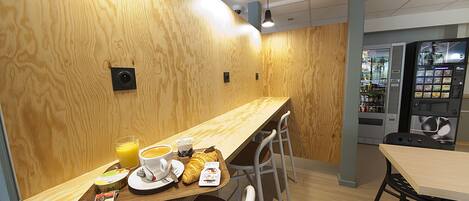 Een houten interieur met een lange toonbank, stoelen, een automaat en een koffieapparaat.