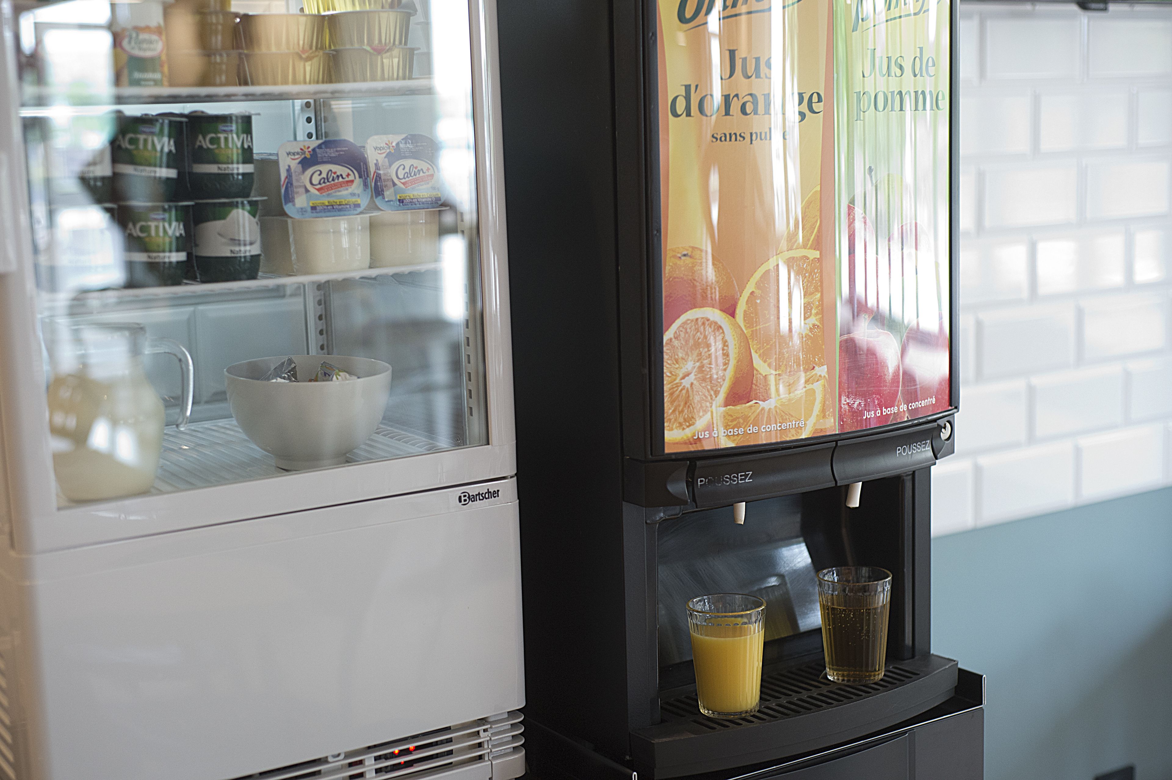Un dispensador de bebidas con un vaso de zumo de naranja y un refrigerador lleno de productos lácteos.