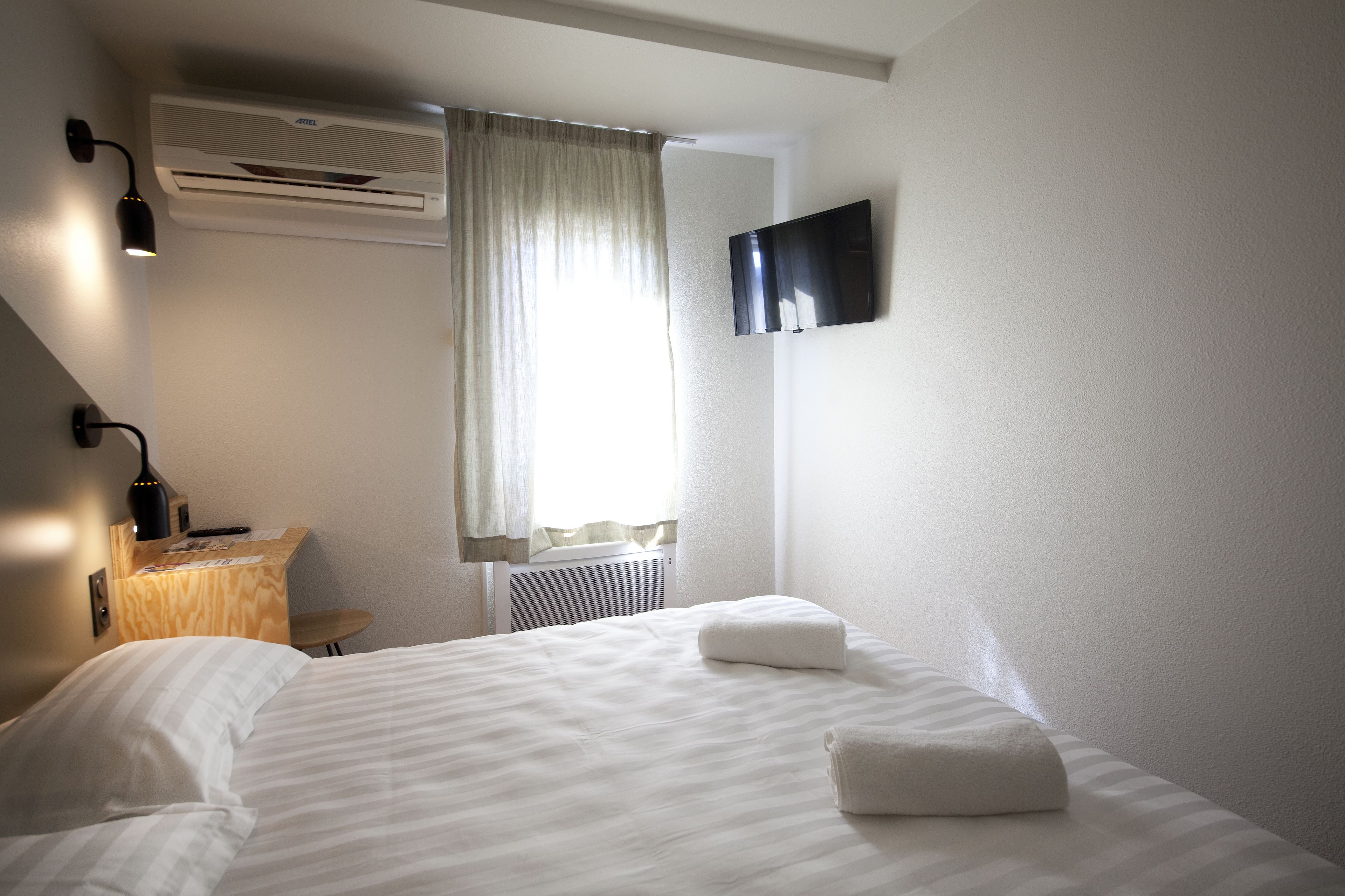 Habitación de hotel con cama, escritorio, silla, aire acondicionado, televisor y ventana con cortinas.