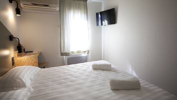 Habitación de hotel con cama, escritorio, silla, aire acondicionado, televisor y ventana con cortinas.