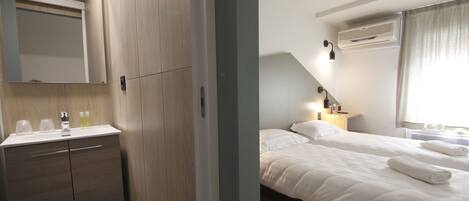 A hotel room with a wooden wardrobe, a bedside table with a lamp, and a bed with white linens and towels.