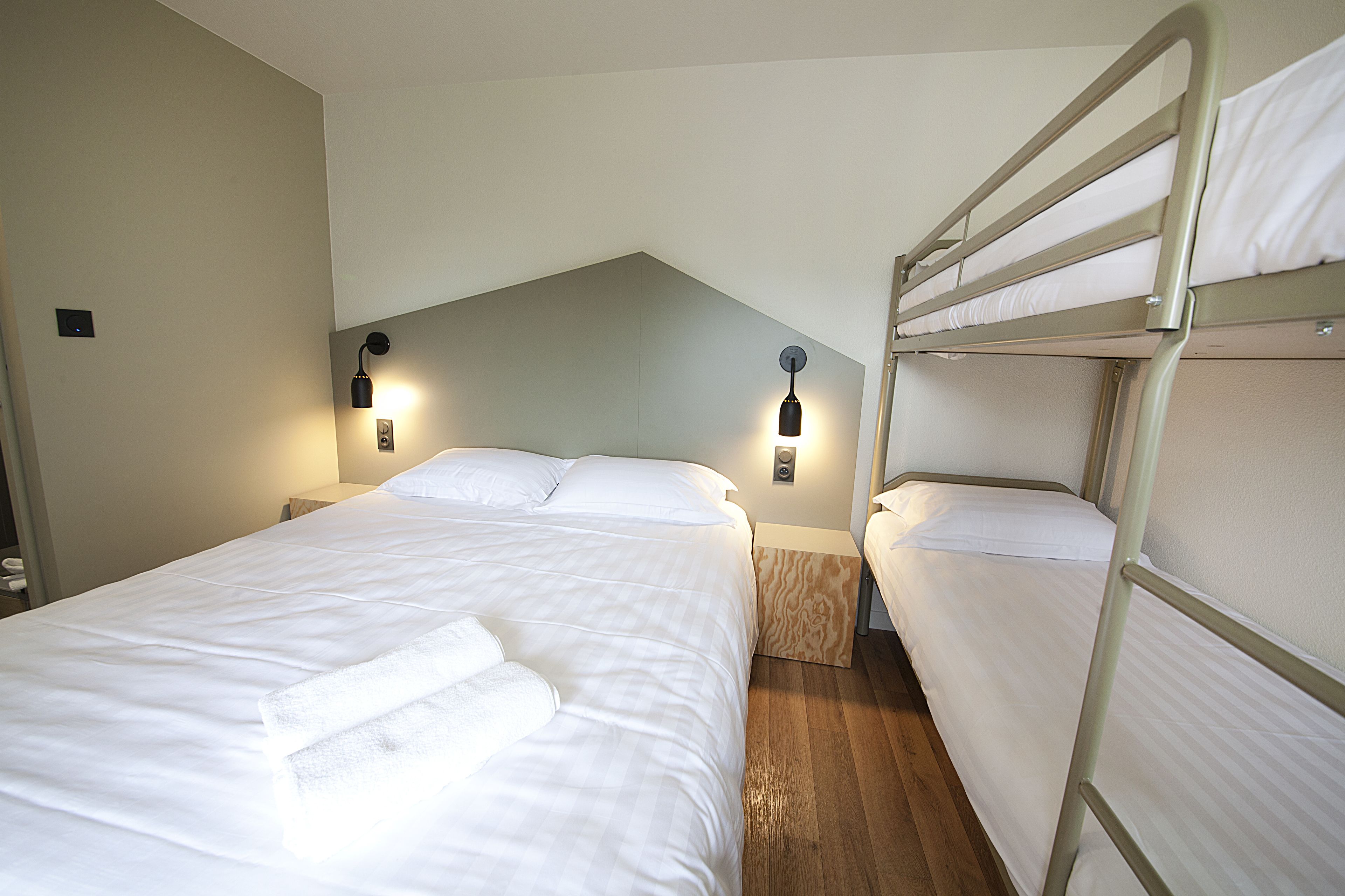 Une chambre d’hôtel avec un lit superposé, un lit simple et deux lampes de chevet.