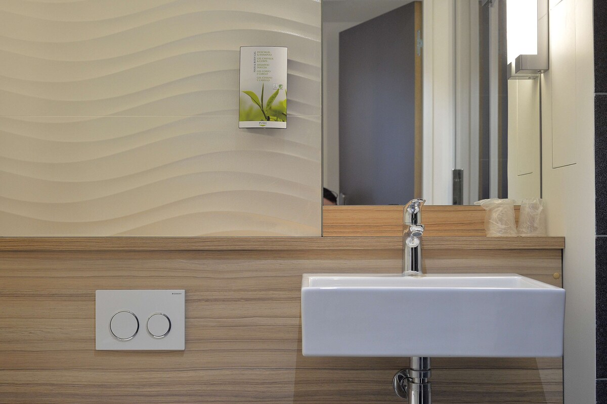 Casa de banho moderna com lavatório branco, painéis de madeira, termostato fixado na parede e espelho com luz.
