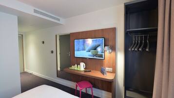 Ein Hotelzimmer mit einem Bett, einem Schreibtisch mit Fernseher, einem Kleiderständer und einem Schrank.
