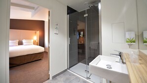A modern hotel room with a bed, a shower, and a sink.
