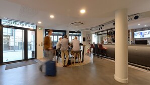 A modern hotel lobby with a reception desk, seating area, and a bar/lounge.