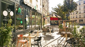 Un hotel con un letrero de 'Camparie', zona de estar al aire libre con mesas y sillas, y un letrero que indica 'Lounge Bar'.