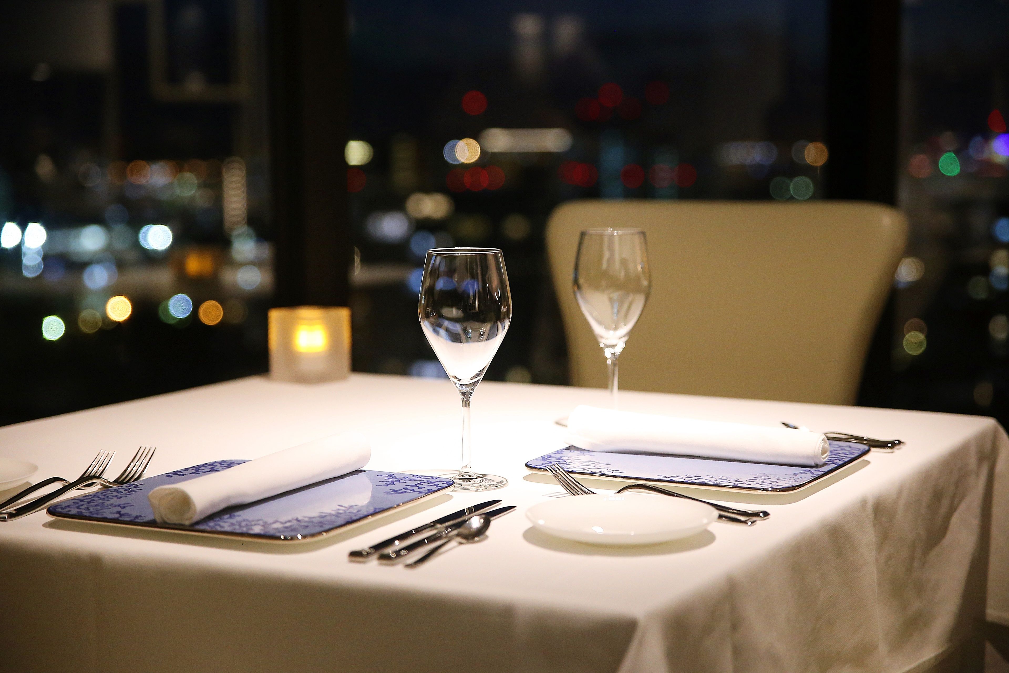A dining table set with white tablecloth, blue patterned placemats, and two wine glasses.