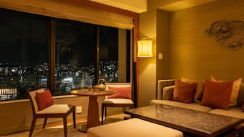 A modern hotel room with a city view, a round table, a sofa, and two armchairs.