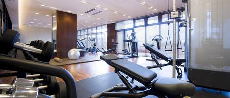 A modern gym with various exercise equipment, large windows, and a clean, well-lit interior.
