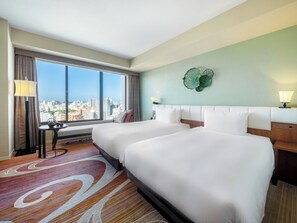A hotel room with two beds, a large window with a city view, a small table with a lamp, and a decorative wall piece. - Hyatt Regency Naha, Okinawa (Naha)