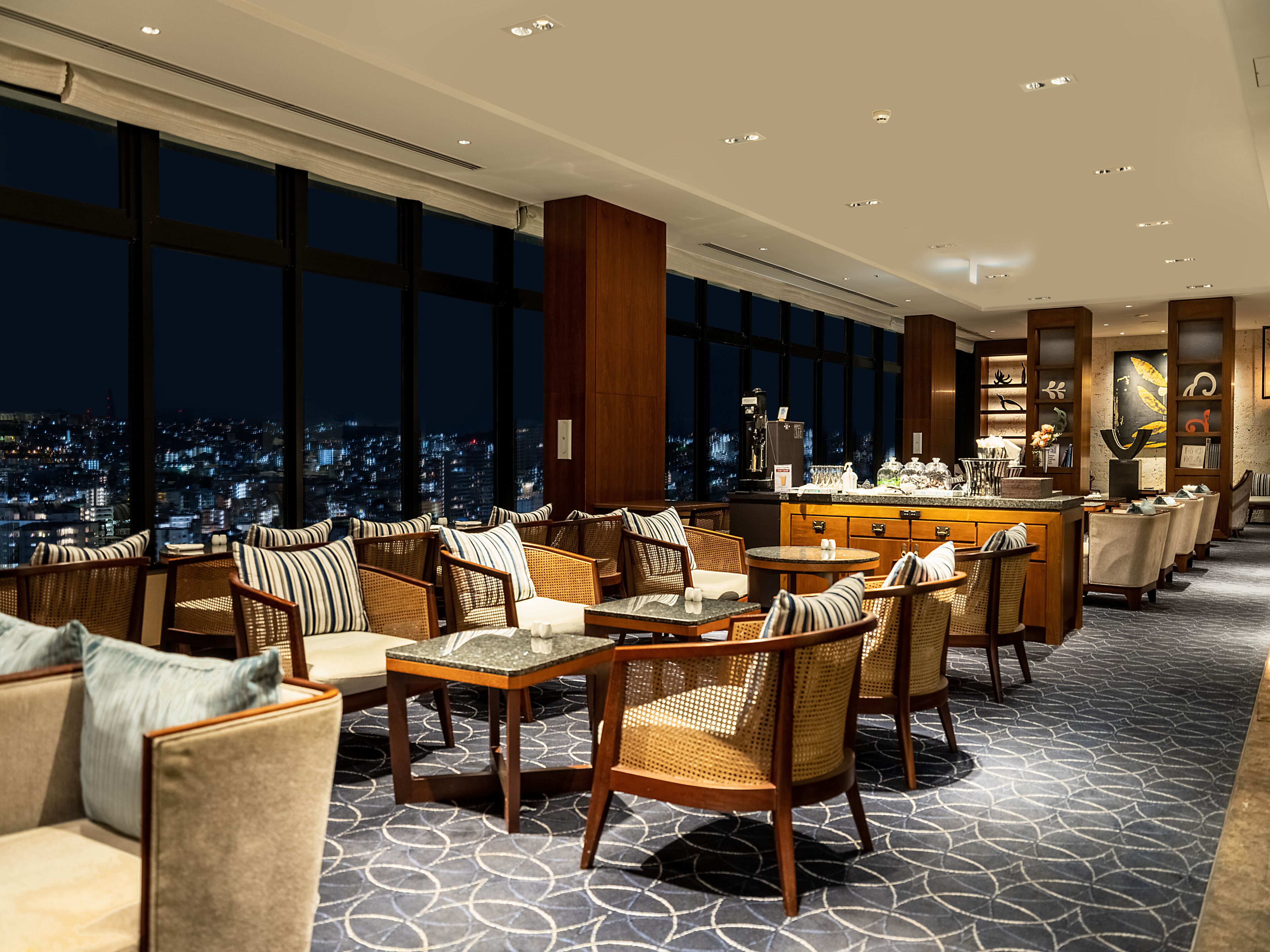 Amplia sala de estar con techos altos, ventanas grandes que ofrecen vistas de la ciudad y un bar con variedad de bebidas y aperitivos.