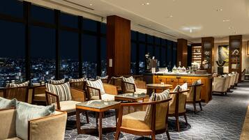 Amplia sala de estar con techos altos, ventanas grandes que ofrecen vistas de la ciudad y un bar con variedad de bebidas y aperitivos.