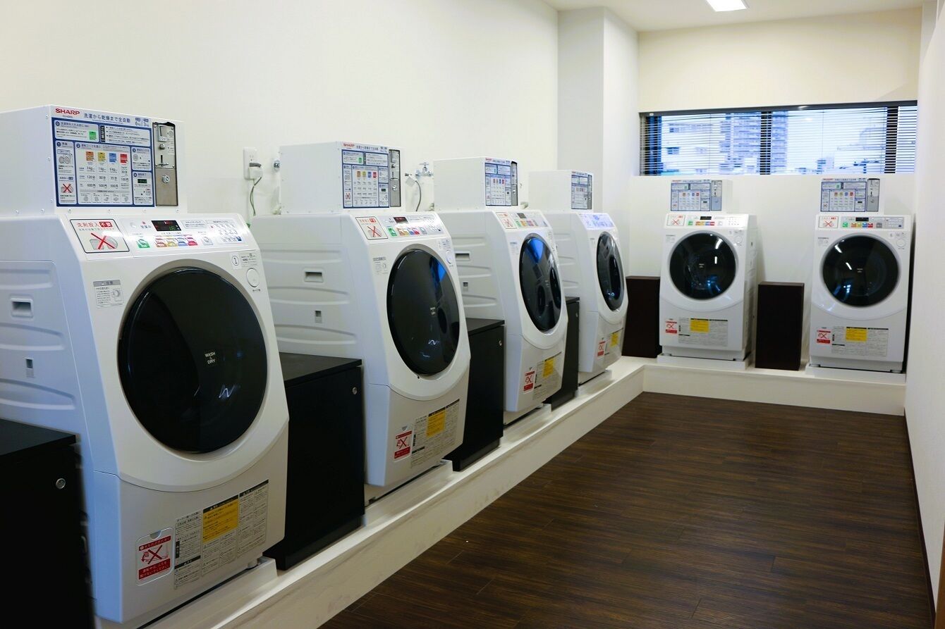 A row of white front-loading washing machines in a room with wooden flooring and a window in the background.