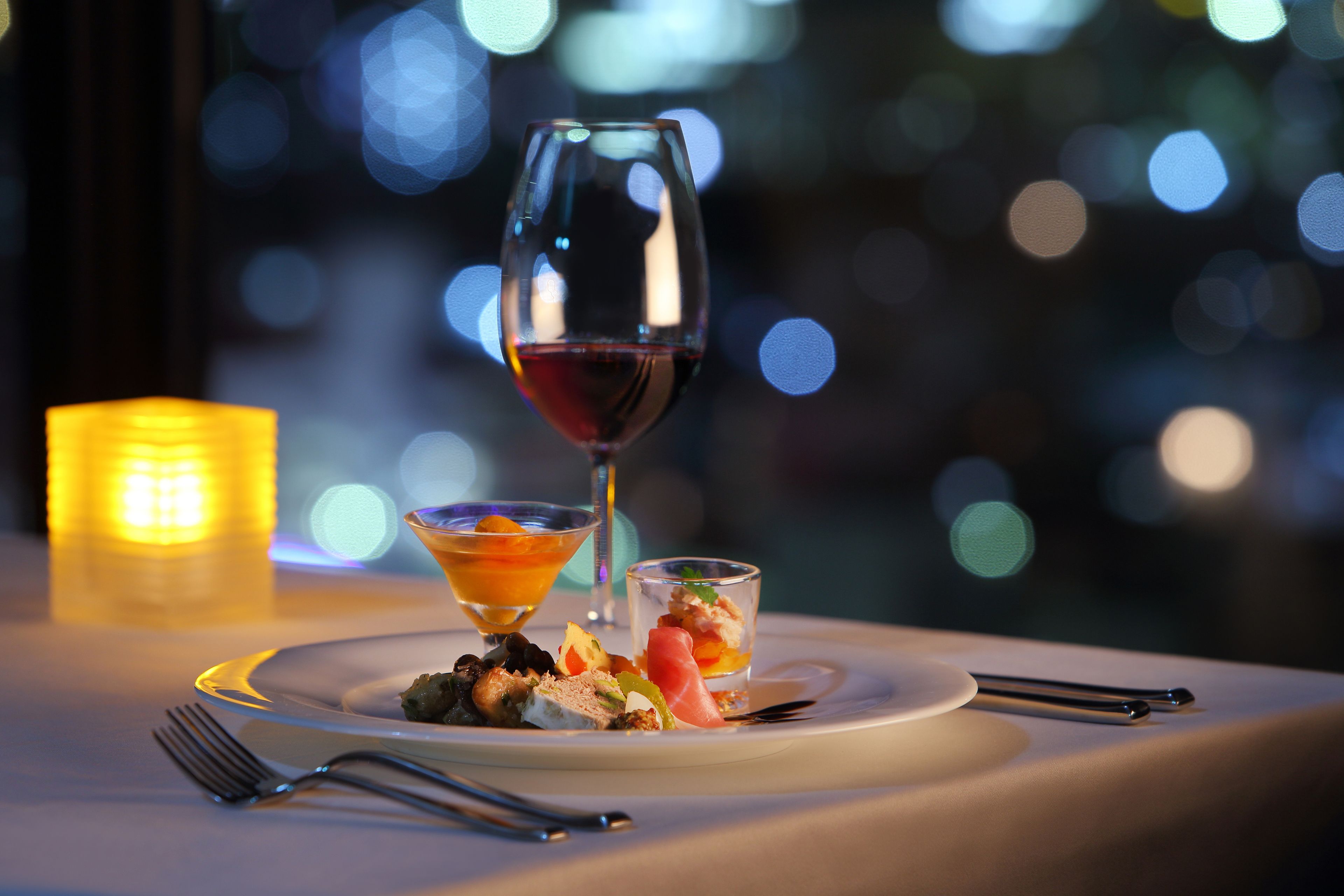 Una mesa dispuesta con una copa de vino, dos vasos de postre pequeños y un plato con comida.