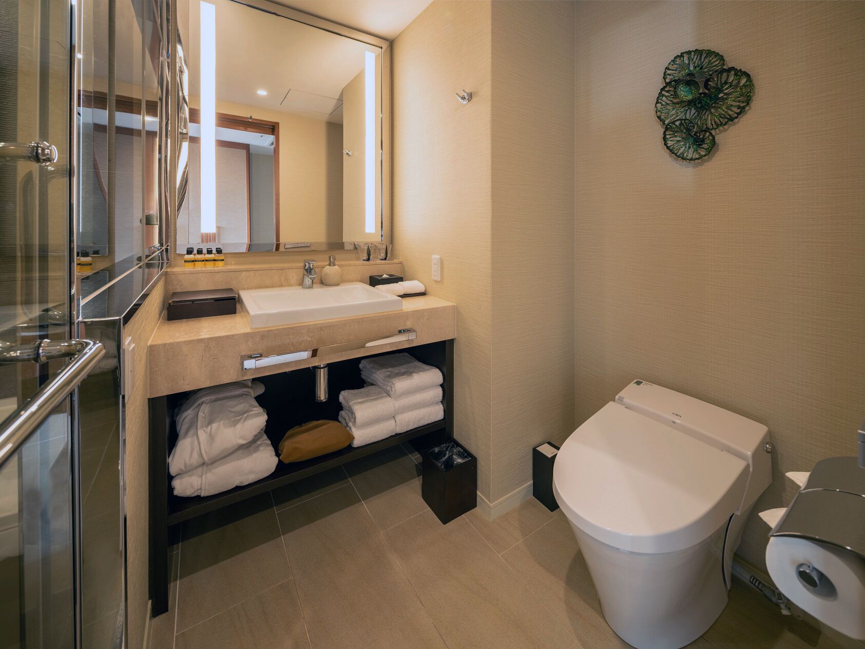 Een moderne badkamer met een douchecabine van glas, een beige wastafel met een wastafel, spiegel en handdoekopslag.