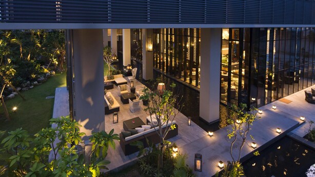 A modern hotel lobby with a pool, outdoor seating, and a view of the interior through large windows.