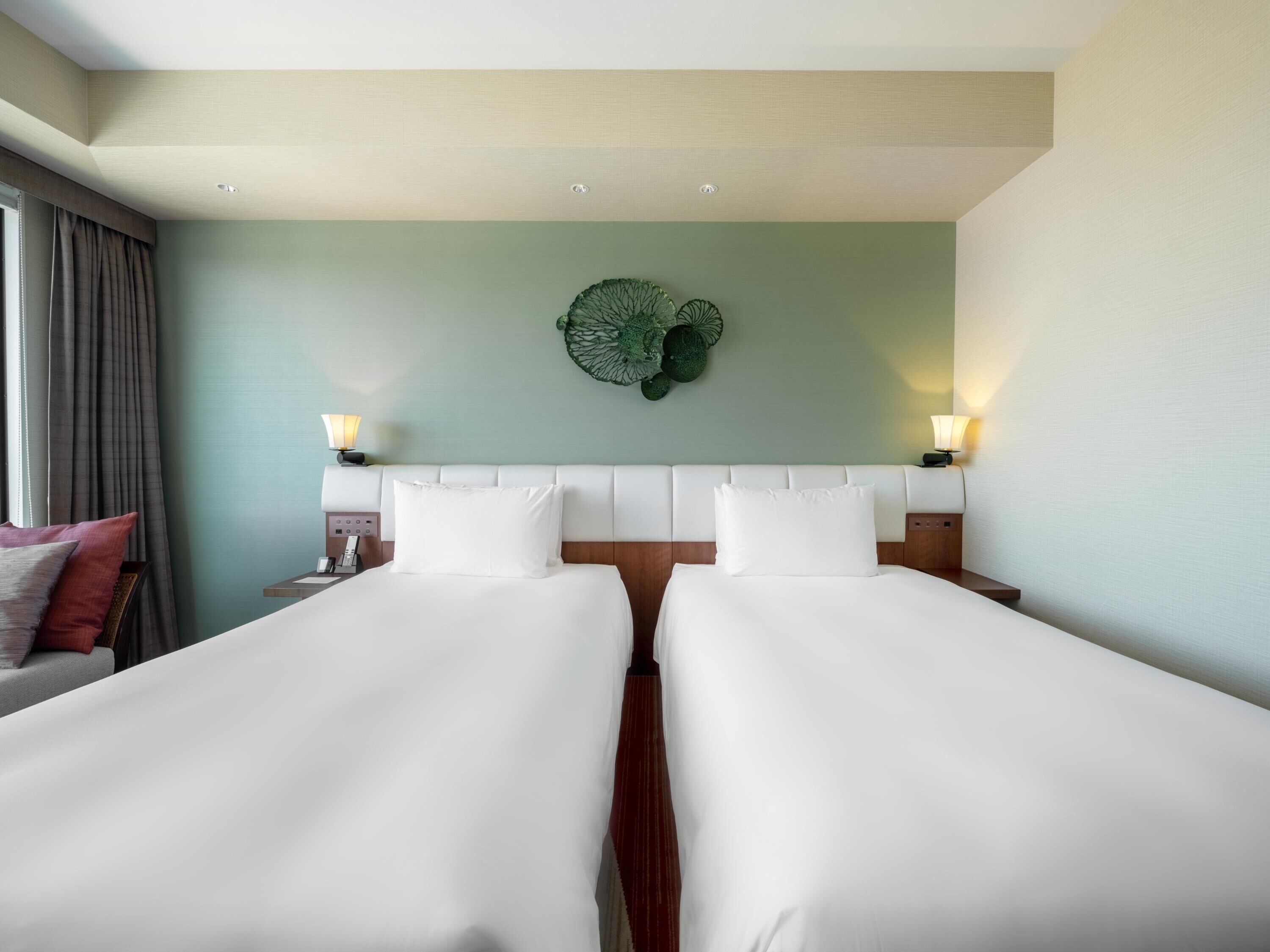 A hotel room with two beds, a green wall, and a decorative wall hanging.