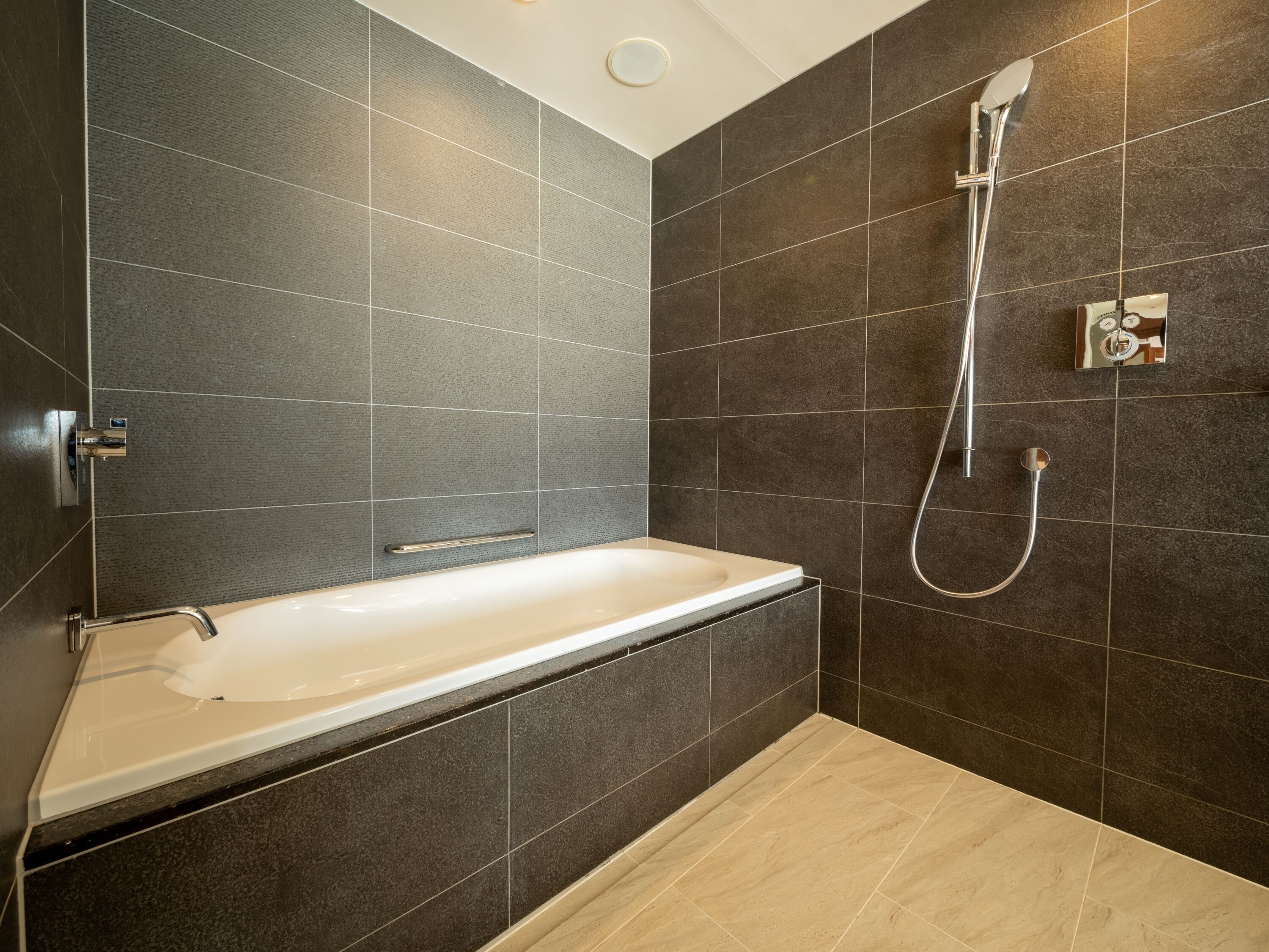 A modern bathroom with a bathtub, a shower, and dark tiled walls.