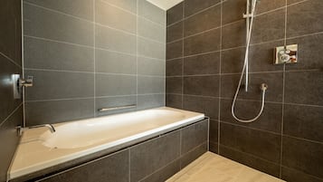 Et moderne badeværelse med badekar, bruser og mørke flisevægge.