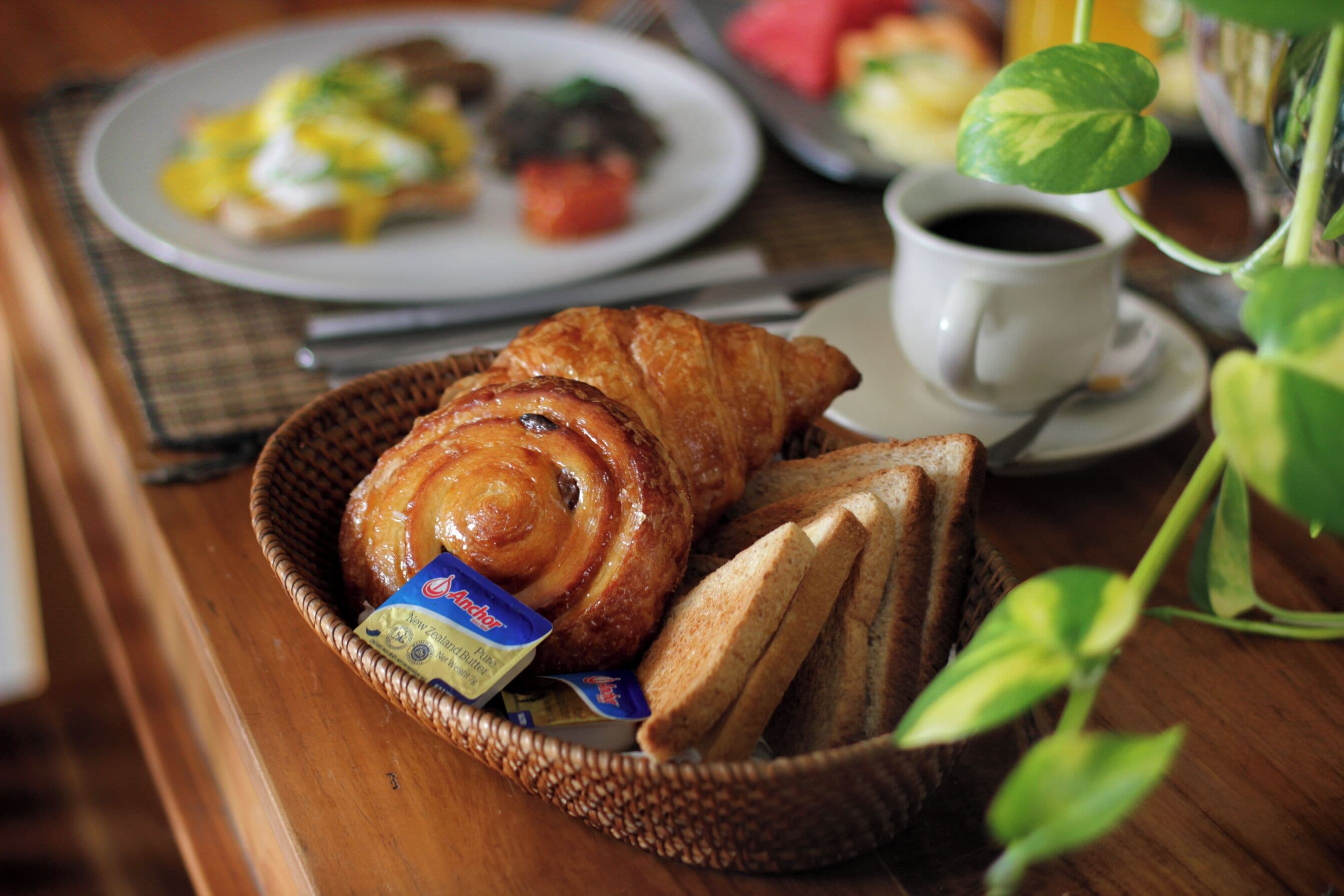 Une table en bois dressée pour le petit-déjeuner, avec un croissant, des toasts et une tasse de café.