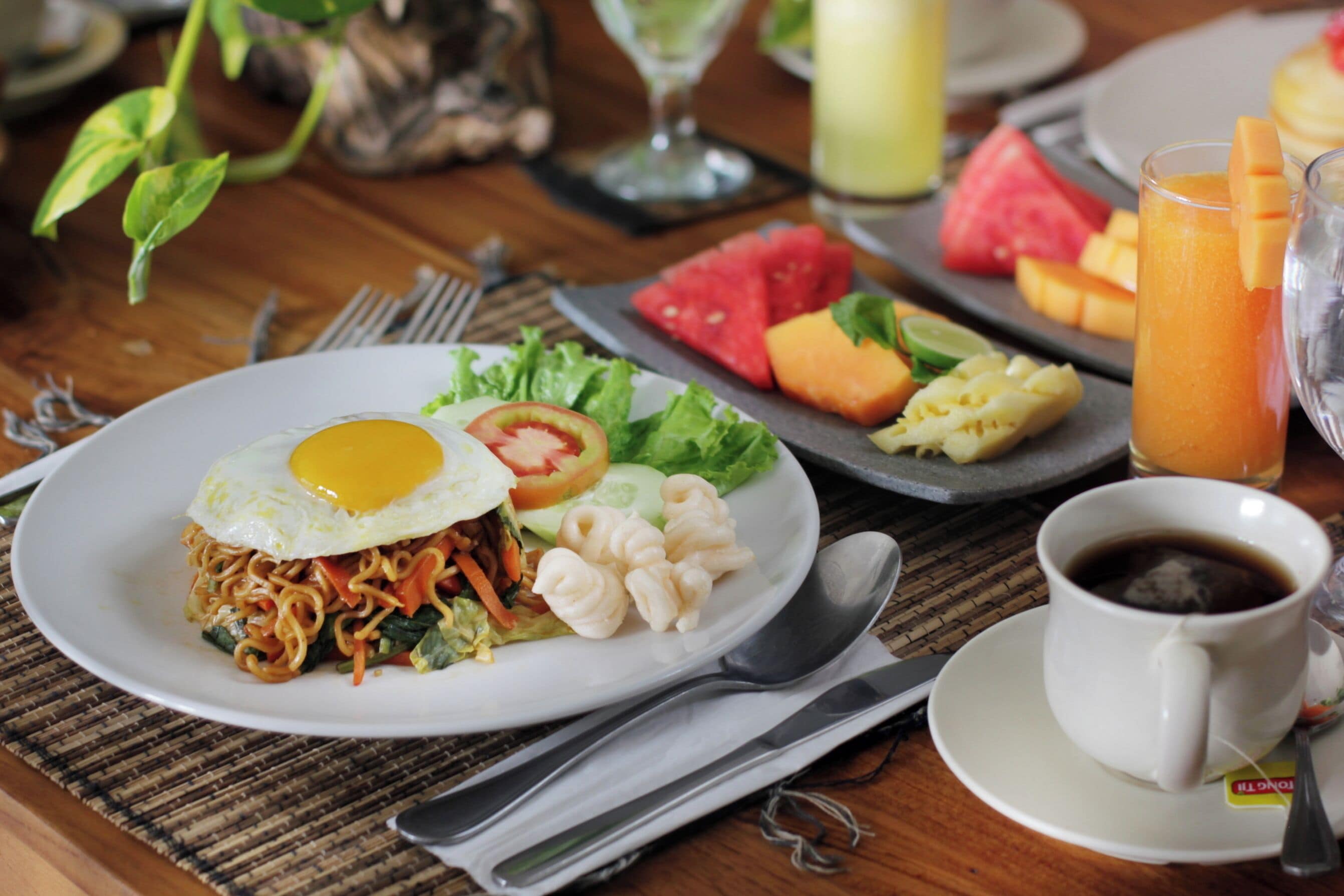 A meal with noodles, vegetables, and a fried egg on a plate, accompanied by a cup of coffee and a glass of orange juice.