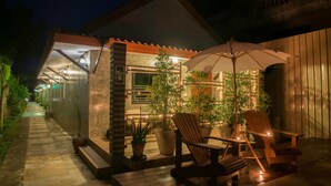 An outdoor patio area with wooden chairs and tables, potted plants, and a large umbrella. - Pai Sukhothai Resort (Sukhothai)