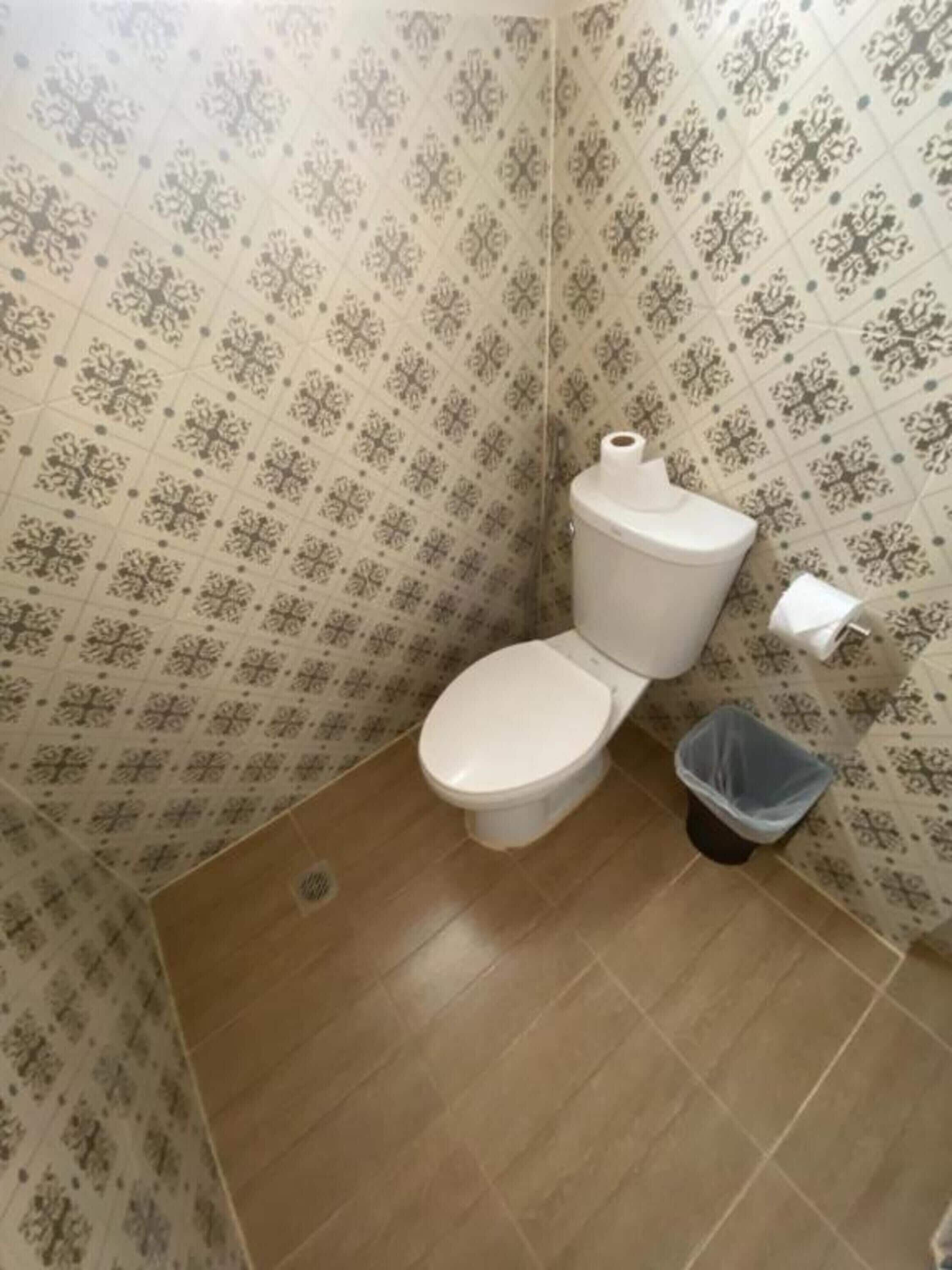 Une petite salle de bain avec des toilettes, une poubelle et un papier peint à motifs.