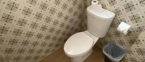 Une petite salle de bain avec des toilettes, une poubelle et un papier peint à motifs.