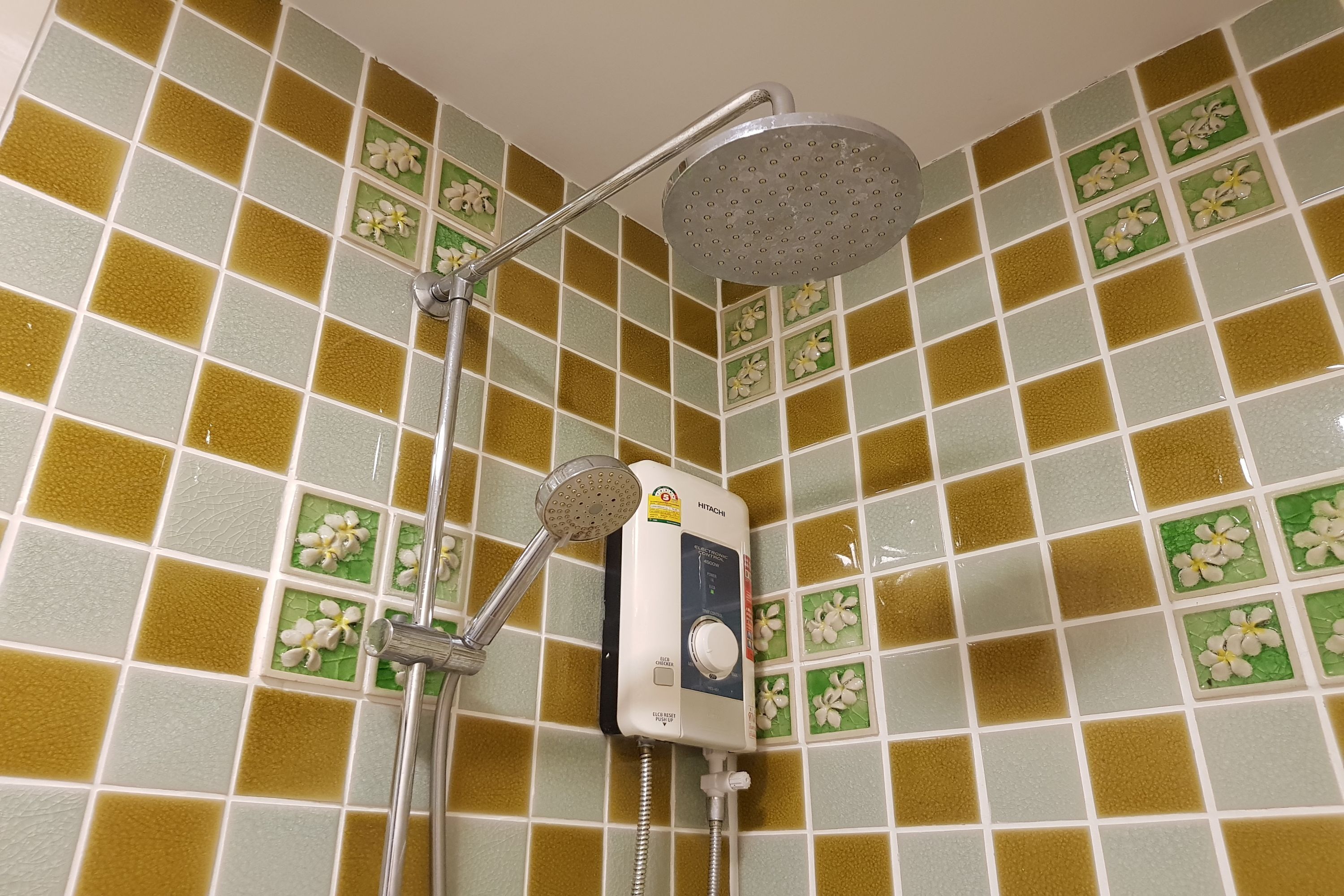 A corner shower with a handheld showerhead and a fixed overhead showerhead, both mounted on a wall with a green and yellow tile pattern.