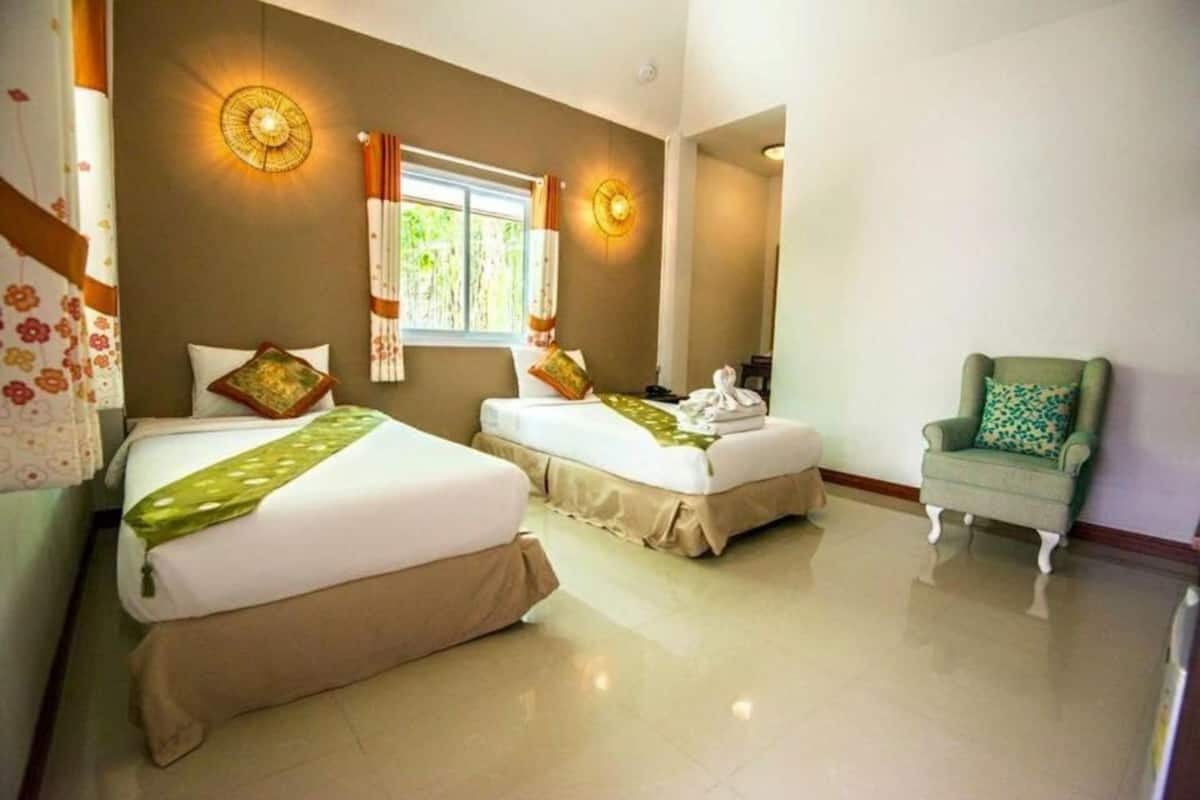 Habitación de hotel con dos camas, una silla y una ventana con cortinas.