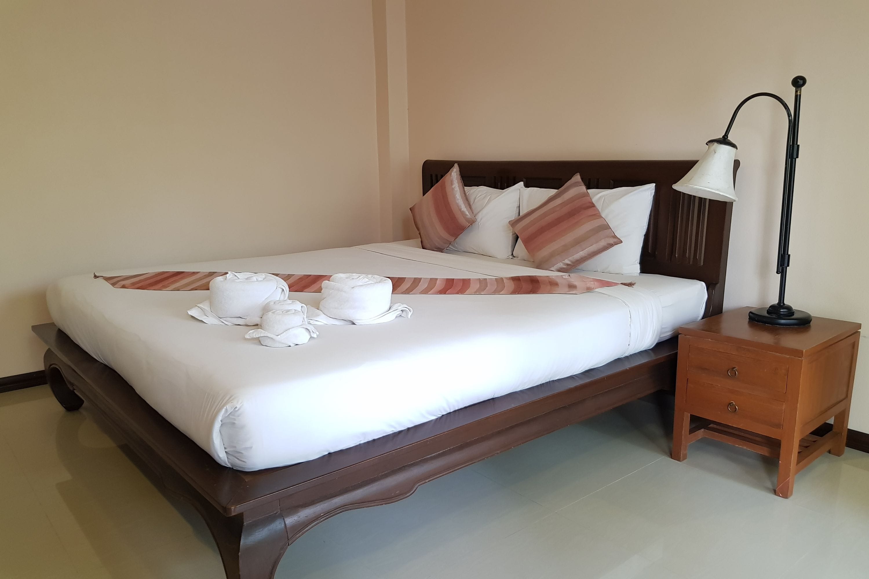 A neatly made bed with white linens and towels, a wooden headboard, and a bedside table with a lamp.