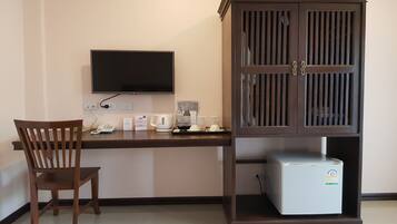 Una habitación con un escritorio de madera, un televisor montado en la pared, un mueble con refrigerador y una silla.