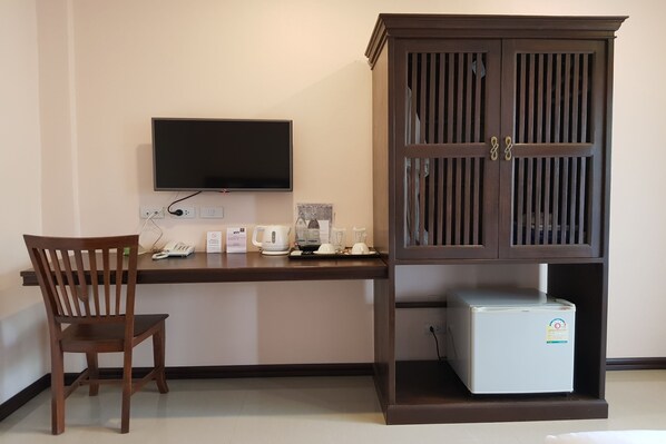 A room with a wooden desk, a television mounted on the wall, a cabinet with a refrigerator, and a chair. - Pai Sukhothai Resort (Sukhothai)