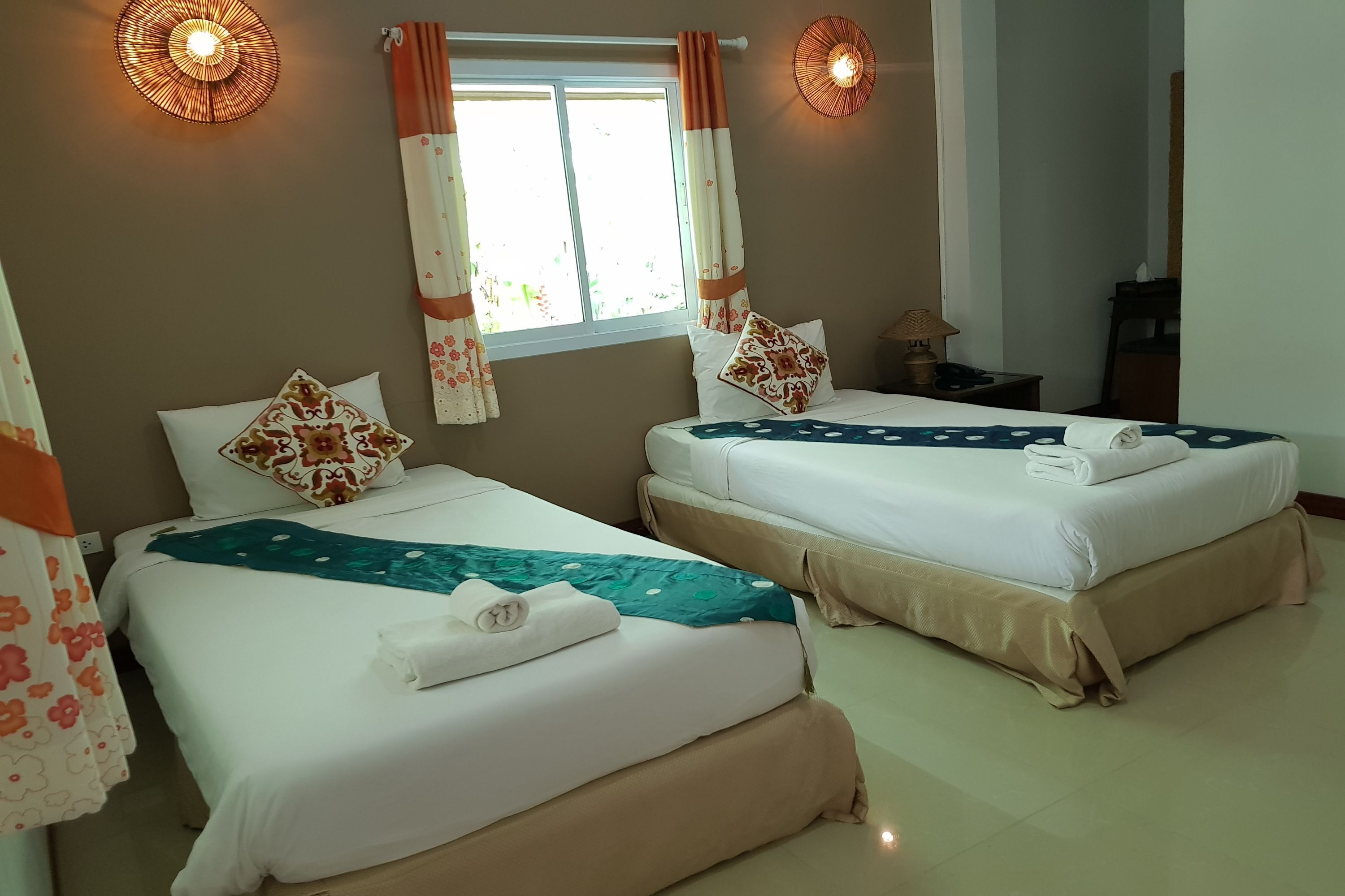 Habitación de hotel con dos camas, una ventana con cortinas, una lámpara de noche y un aplique de pared.